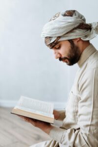 Man in traditional attire peacefully reading Quran indoors, symbolizing Islamic devotion.
